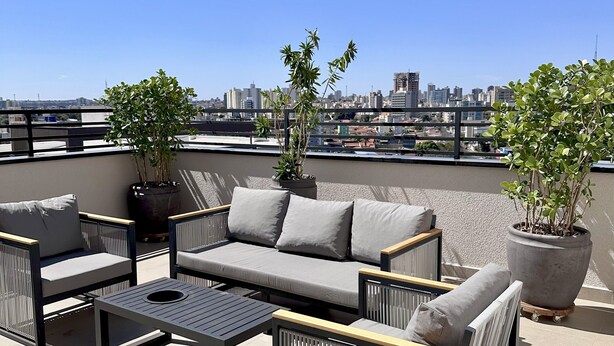 A rooftop terrace with a sofa set, two potted plants, and a view of the city skyline.
