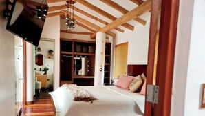 Un dormitorio con techo de madera, una cama con ropa de cama blanca, un espejo y un tocador con lavamanos.
