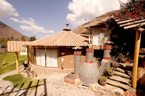 A traditional building with a tiled roof, stone walls, and a wooden porch. - An intimate retreat in the Holy Valley, with views of a waterfall, mountains, a campfire, and a maloka (Arin)