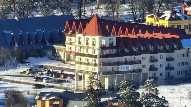 Un hotel de varios pisos con techo rojo, rodeado de árboles cubiertos de nieve y un estacionamiento.