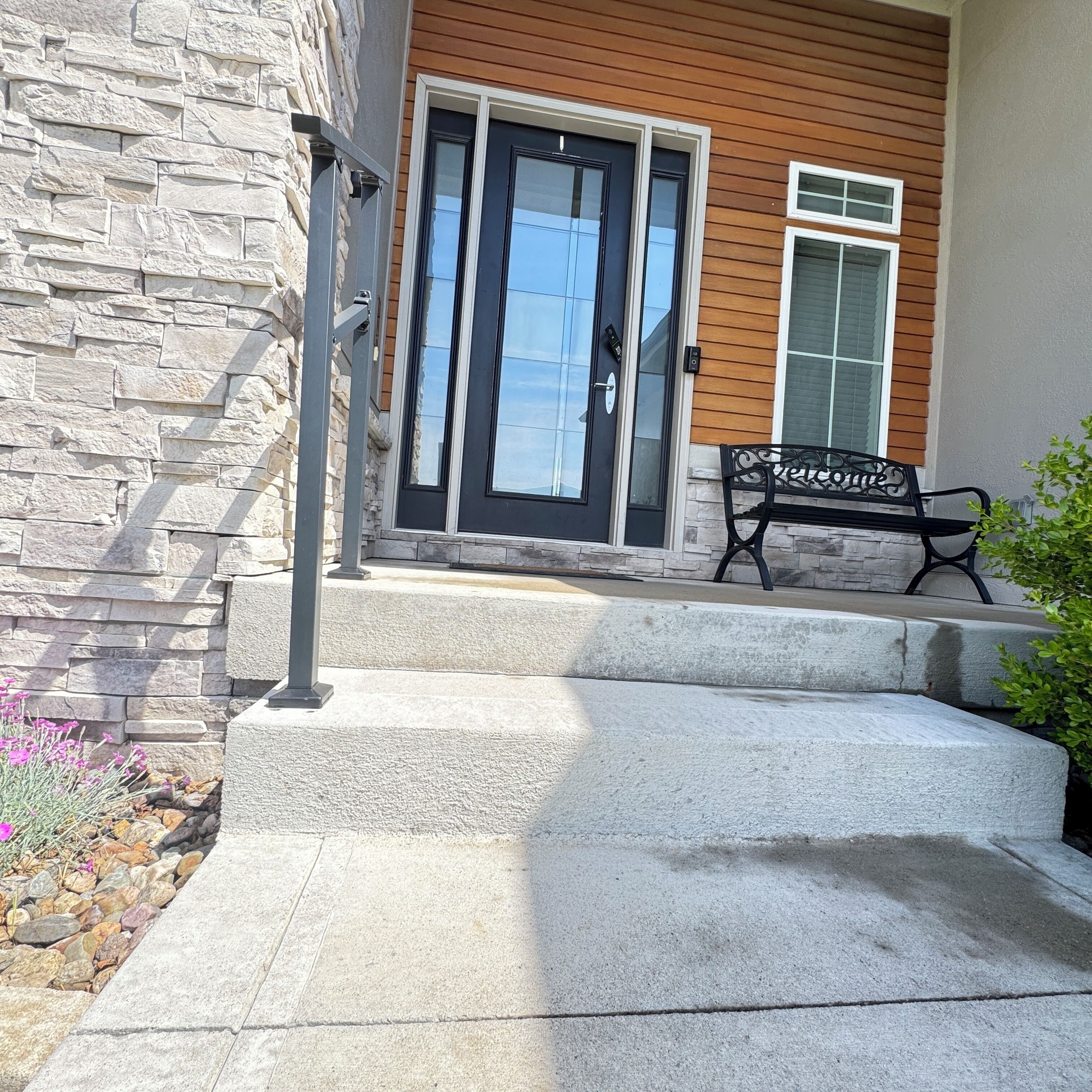 A stone exterior wall, a black door with glass panels, and a bench with a sign.