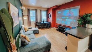 A modern living room with a grey sofa, a dining table, and a large TV screen displaying a movie.