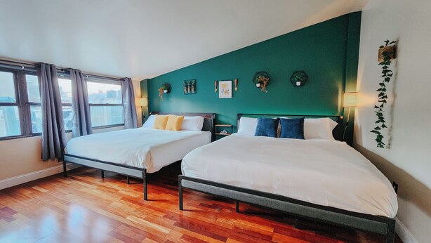 A room with two single beds, wooden flooring, a teal accent wall, and a window with curtains.