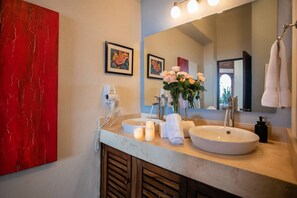 Ein Badezimmer mit zwei Waschbecken, einem Fön, einem Spiegel und einem roten abstrakten Gemälde.