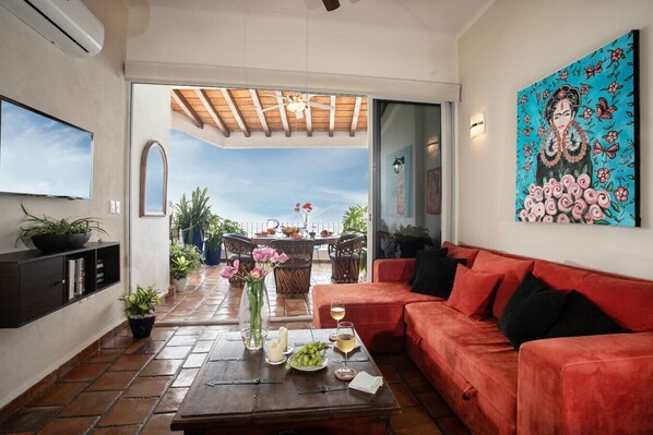 Ein Wohnzimmer mit einem roten Sofa, einem Couchtisch mit Getränken und Blumen, einem Fernseher und einem Bild an der Wand.