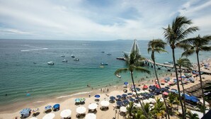 A beach with palm trees, a pier, and boats on the water.