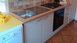 Una cocina con estufa a gas, lavamanos y cafetera.