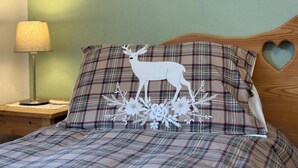 Una cama con ropa de cama escocesa, un almohadón con diseño de ciervo y flores, y un recorte en forma de corazón en la cabecera.