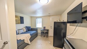 A compact living space with a sofa, a small table, a refrigerator, and a TV mounted on the wall. - Inclinescape#3 (Colorado Springs)