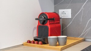 En röd kaffemaskin på ett träbricka, tillsammans med två koppar och tre kaffekapslar.