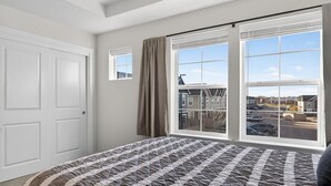 A bedroom with a large bed, a window with curtains, and a view of buildings outside.
