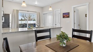 A modern kitchen with a central island, pendant lighting, and a dining area with a wooden table and chairs.