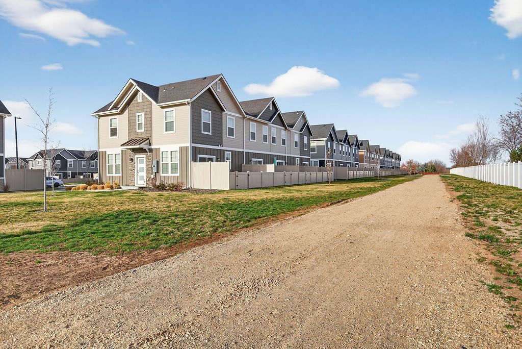 A row of townhouses with a gravel driveway, a fenced area, and a clear sky.