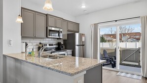 A modern kitchen with granite countertops, stainless steel appliances, and a sliding glass door leading to a patio.
