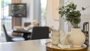 A dining table with a white vase, a white ceramic mug, and a white ceramic sculpture on a wooden tray.