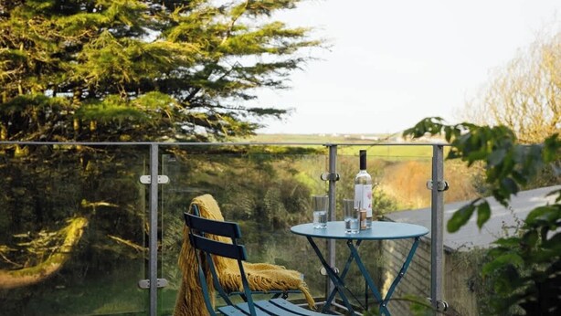 Ein Balkon mit Tisch und Stuhl, umgeben von Glasgeländern, mit Blick auf eine natürliche Landschaft.
