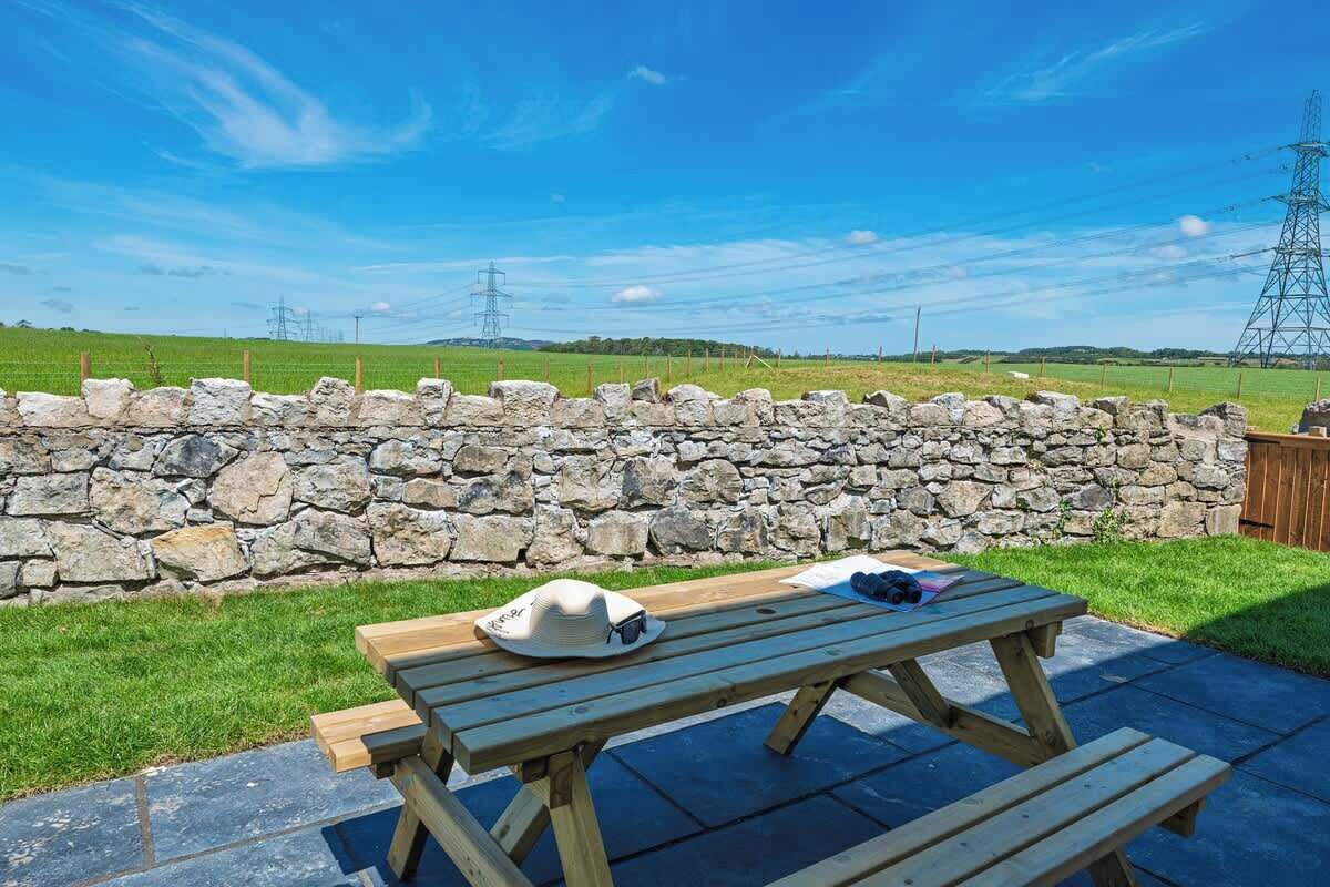 A stone wall, a picnic table, and a grassy field with power lines in the background.