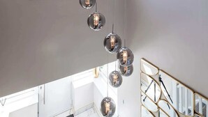 Un intérieur moderne, avec une longue rangée de luminaires sphériques suspendus, une grande fenêtre donnant sur un paysage verdoyant et un escalier doté d’une rampe au design géométrique.