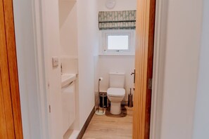 Ein schmaler Flur, der zu einem Badezimmer mit Toilette, Bidet und einem Fenster über der Toilette führt.
