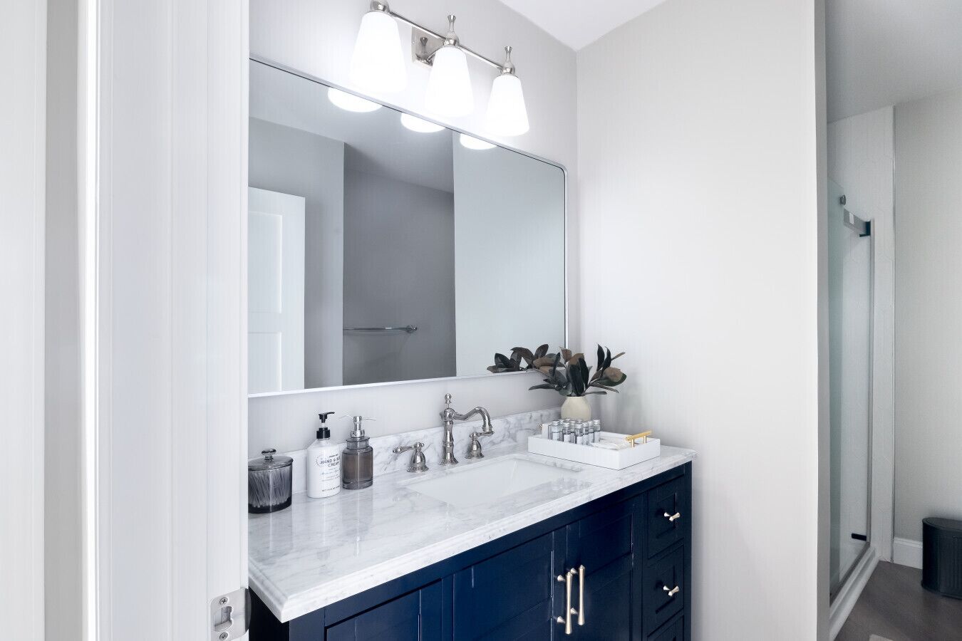 Une salle de bain moderne avec un grand miroir, deux vasques et un meuble-lavabo bleu foncé.
