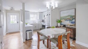 Een moderne keuken met witte kastjes, een centraal eiland en een eethoek met een ronde tafel en stoelen.