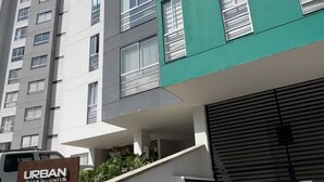 A multi-story residential building with a mix of white and green facades, multiple windows, and a visible entrance area with a sign.