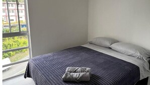 A bedroom with a large window, a bed with a dark blue quilt, and a grey pillow.