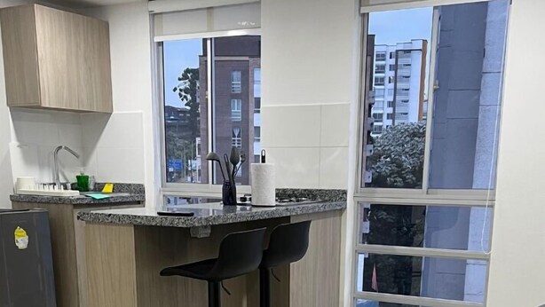 A modern kitchen with a central island, two bar stools, and a large window offering a city view.
