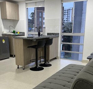 A modern kitchen with a central island, two bar stools, and a large window offering a city view.