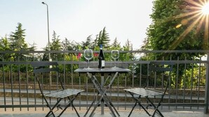 Un patio al aire libre con una mesa y sillas de metal, dos copas de vino y una botella.
