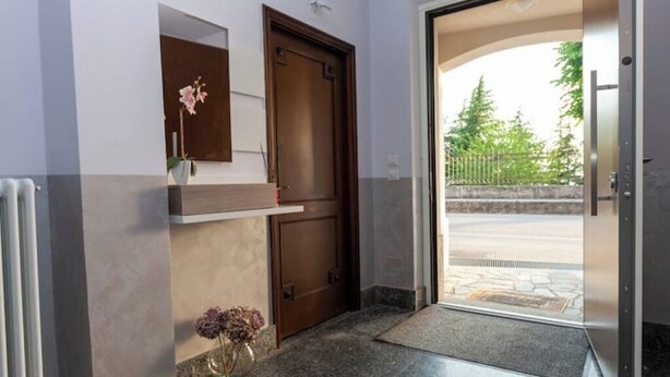 Entrada de un hotel con puerta de madera, un pequeño estante con flores y vista a la calle.