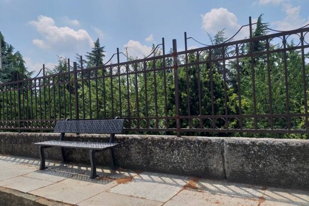 A bench by a metal fence with trees in the background.