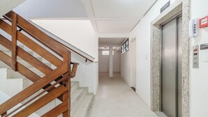 A hotel hallway with a wooden staircase, an elevator, and a wall-mounted phone.