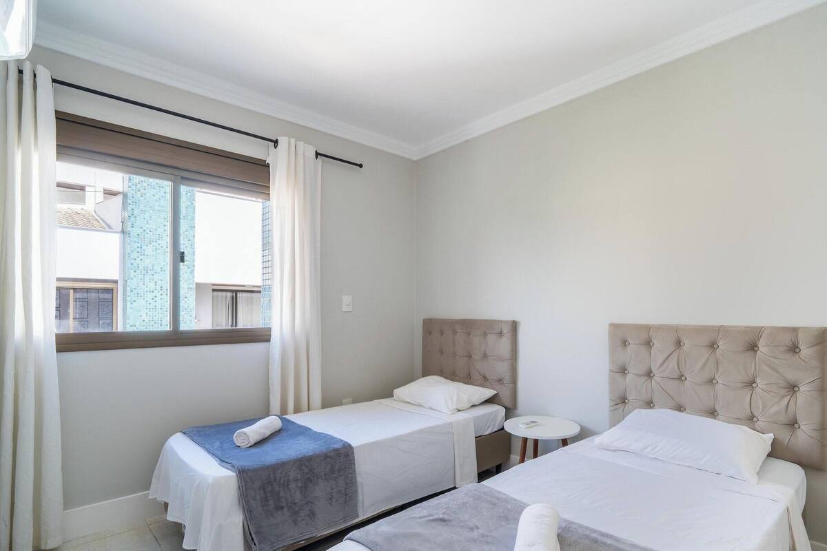Une chambre d’hôtel avec deux lits simples, une petite table ronde et une fenêtre avec des rideaux.