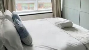 Une chambre avec une grande fenêtre, un lit avec des oreillers et un mur orné de tableaux.