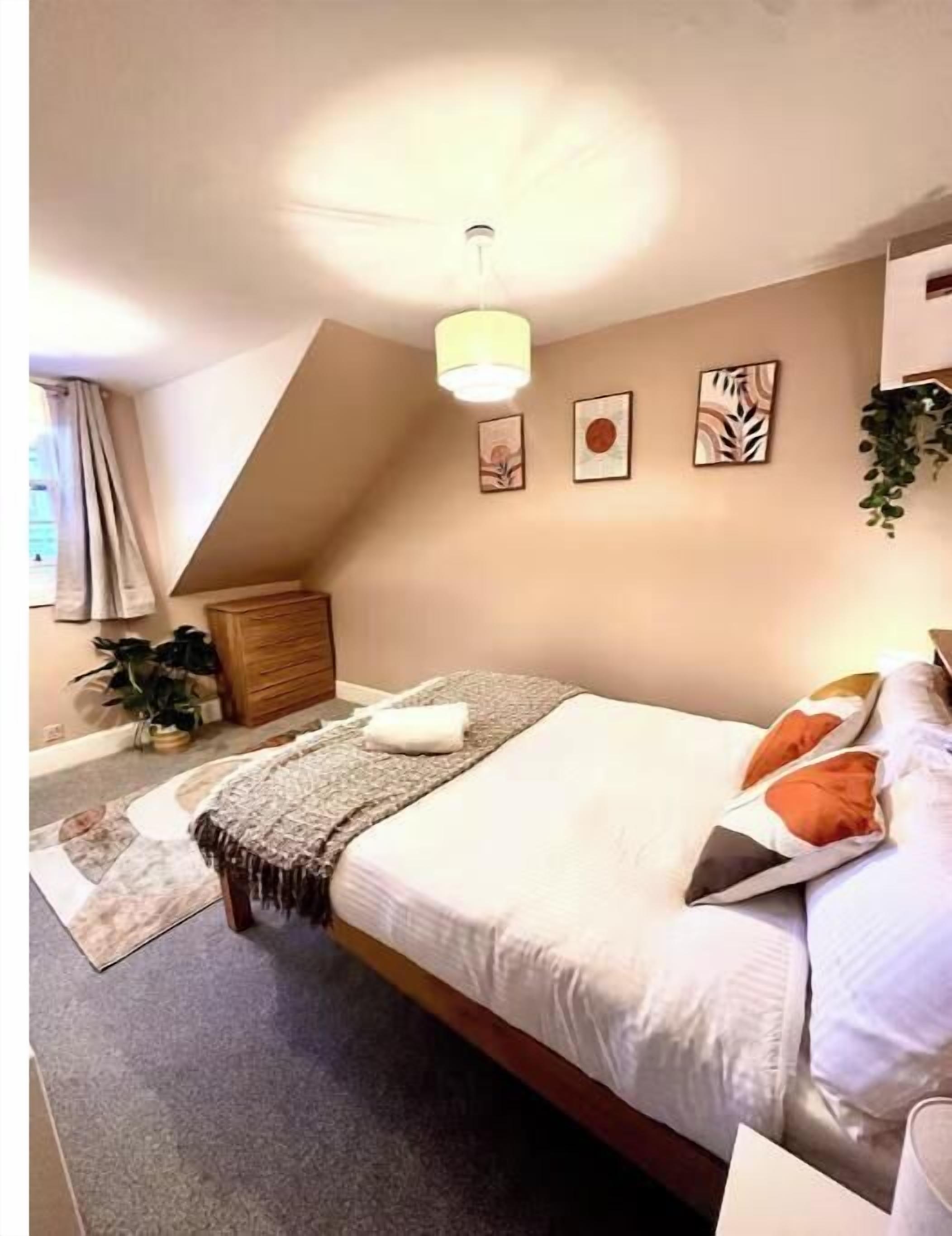A bedroom with a bed, a bedside table, a lamp, a dresser, and a window with curtains.