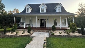 Une maison à deux étages avec un porche à l’avant, des fondations en pierre et une pelouse bien entretenue.