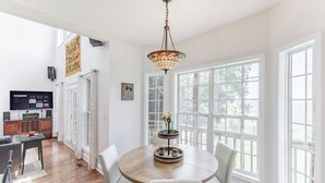 Un espace repas comprenant une table ronde, des chaises, un lustre et une vue sur l’extérieur grâce à de grandes fenêtres.