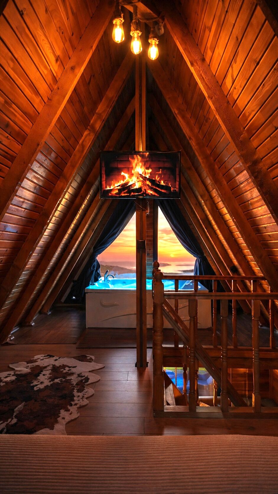 Ein Dachzimmer mit Kamin, Fernseher und Blick auf den Sonnenuntergang.
