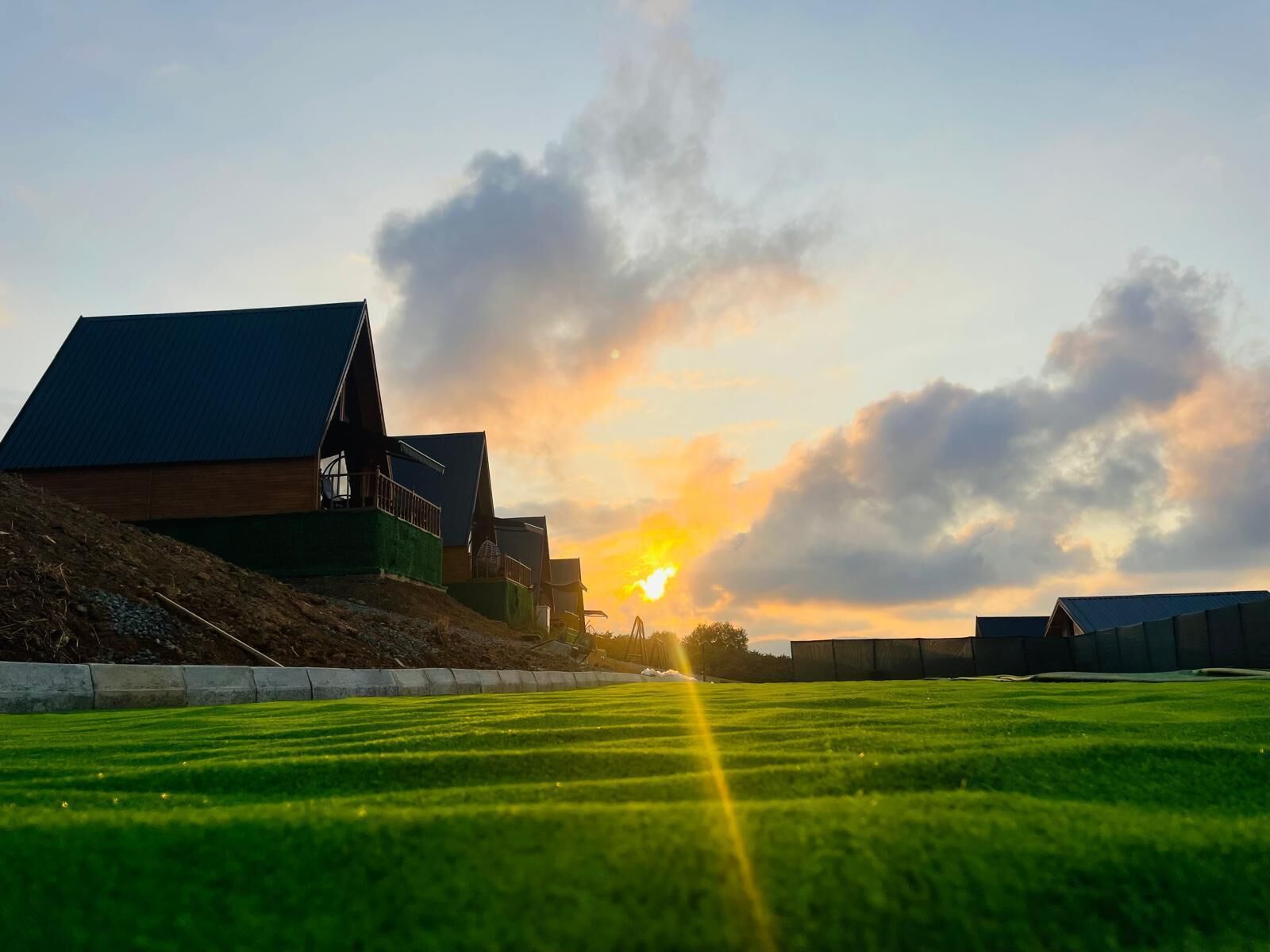 A grassy field with a building and a sunset in the background.