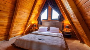 A cozy attic bedroom with a wooden sloped ceiling, a large bed with white linens, two bedside tables with lamps, and a window with curtains. - Galaxy Bungalov (Akçaabat)