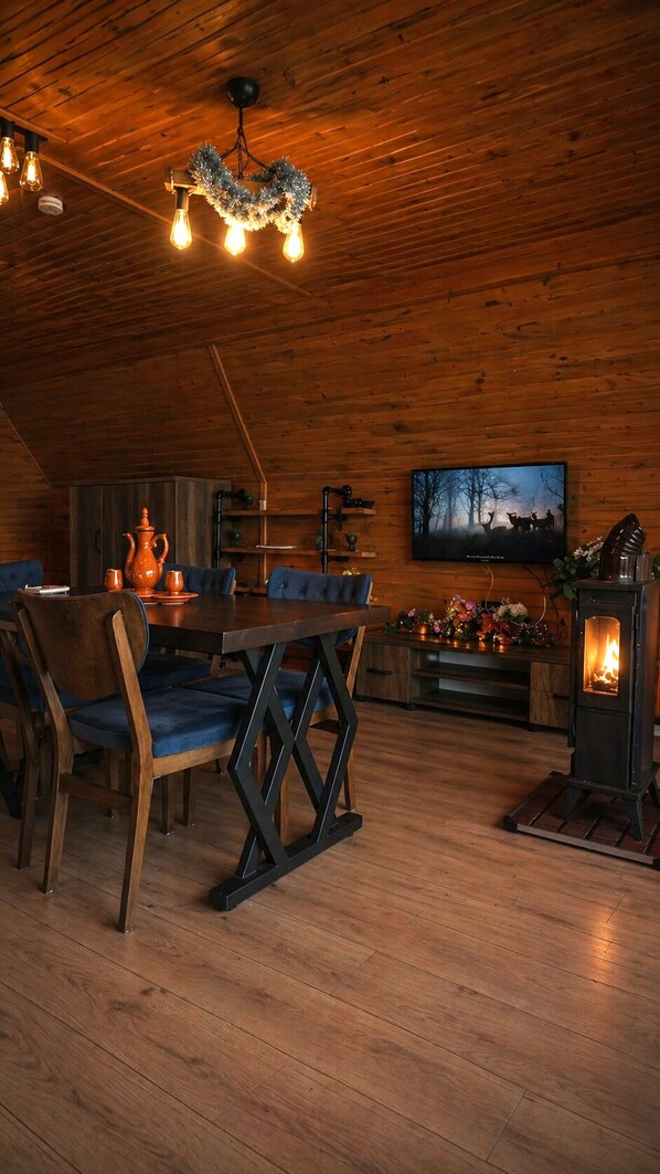 Una habitación acogedora con techo de madera, una mesa de comedor con sillas, un televisor y una chimenea.