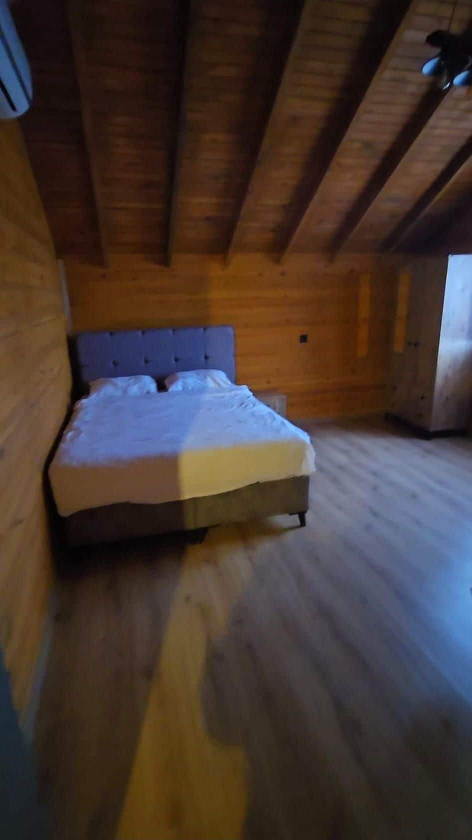 Un dormitorio con techo de madera y una cama con colchón blanco y cabecera azul.
