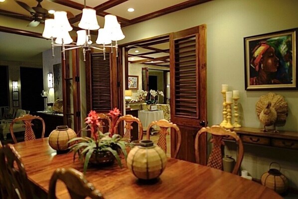 A dining area with a wooden table, chairs, and a chandelier. There are decorative items on the table and a painting on the wall.