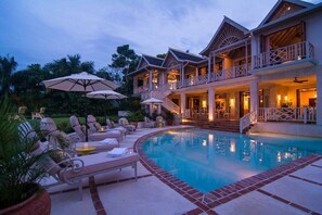 A large, two-story house with a swimming pool, outdoor seating, and a well-lit entrance.