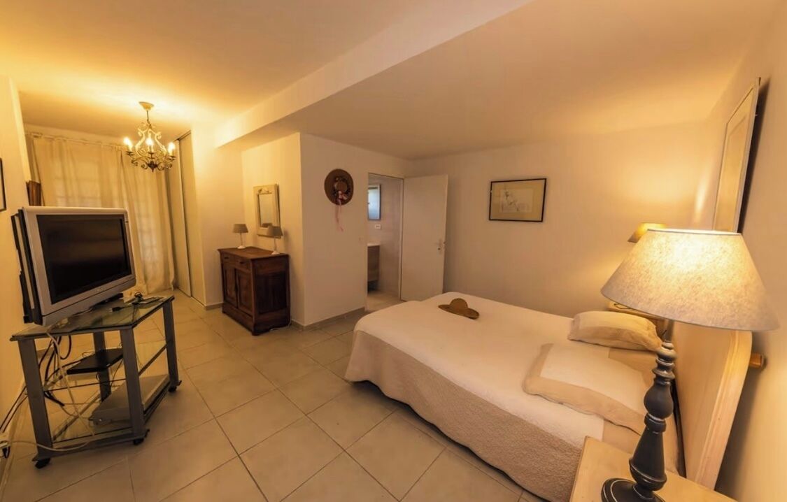 Une chambre d’hôtel avec un lit, un téléviseur posé sur un meuble, une lampe et une porte donnant sur une autre pièce.