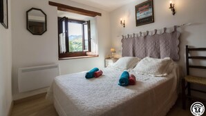 A bedroom with a large bed, a window with curtains, a wall-mounted mirror, a bedside table with a lamp, and a poster on the wall. - L'Edelweiss - Poubeau (Poubeau)