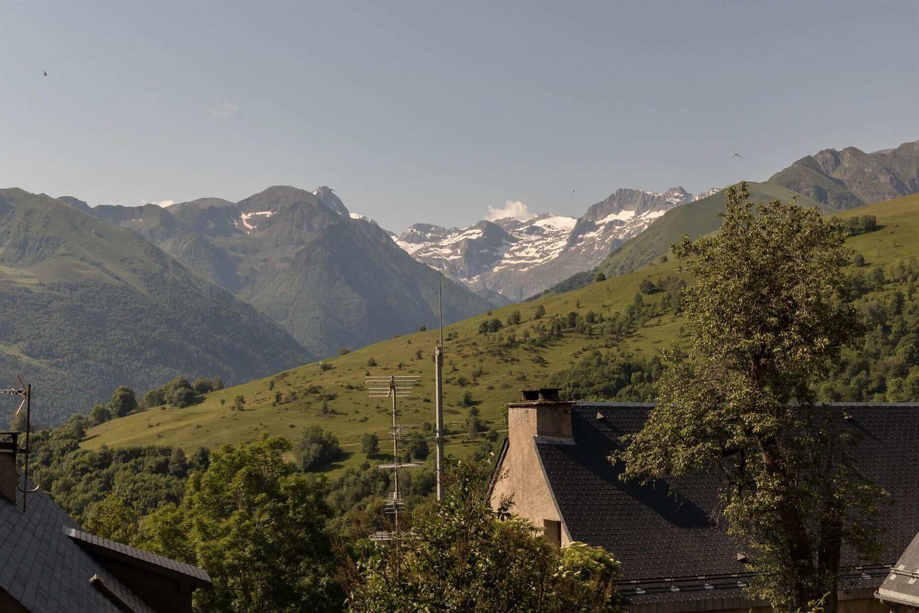 Un paysage montagneux avec une maison dotée d’un toit en pente et d’une cheminée bien visible.
