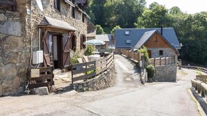 A stone building with a wooden porch, a small wooden structure, and a paved path. - L'Edelweiss - Poubeau (Poubeau)