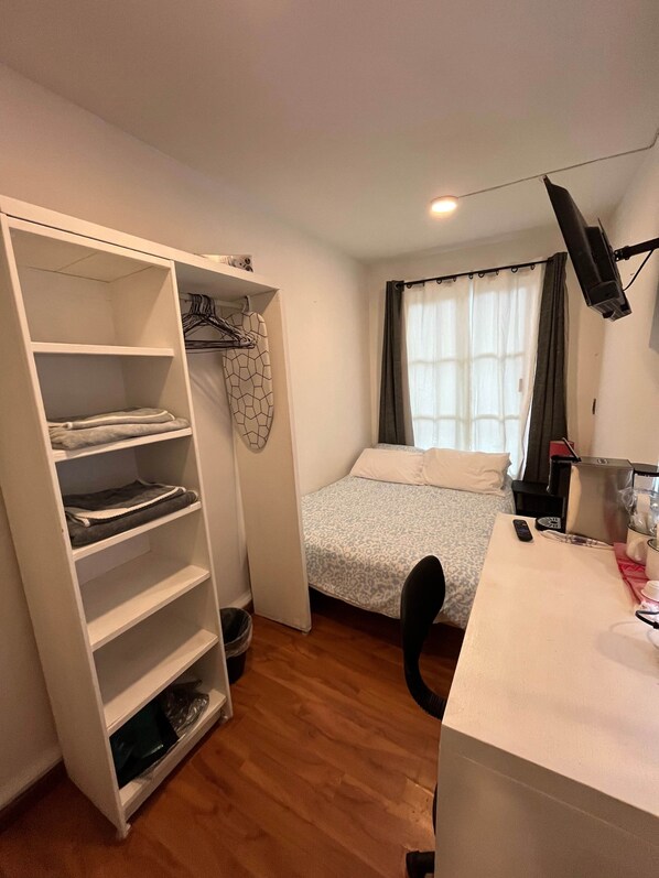 Un dormitorio con cama, escritorio, armario y ventana con cortinas.